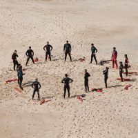 Übungsgruppe von Surfern steht am Strand im Kreis