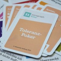 Das Titleblatt des Toleranz-Poker Spiels liegt zentral auf einem wild gemischten Haufen anderer Karten.